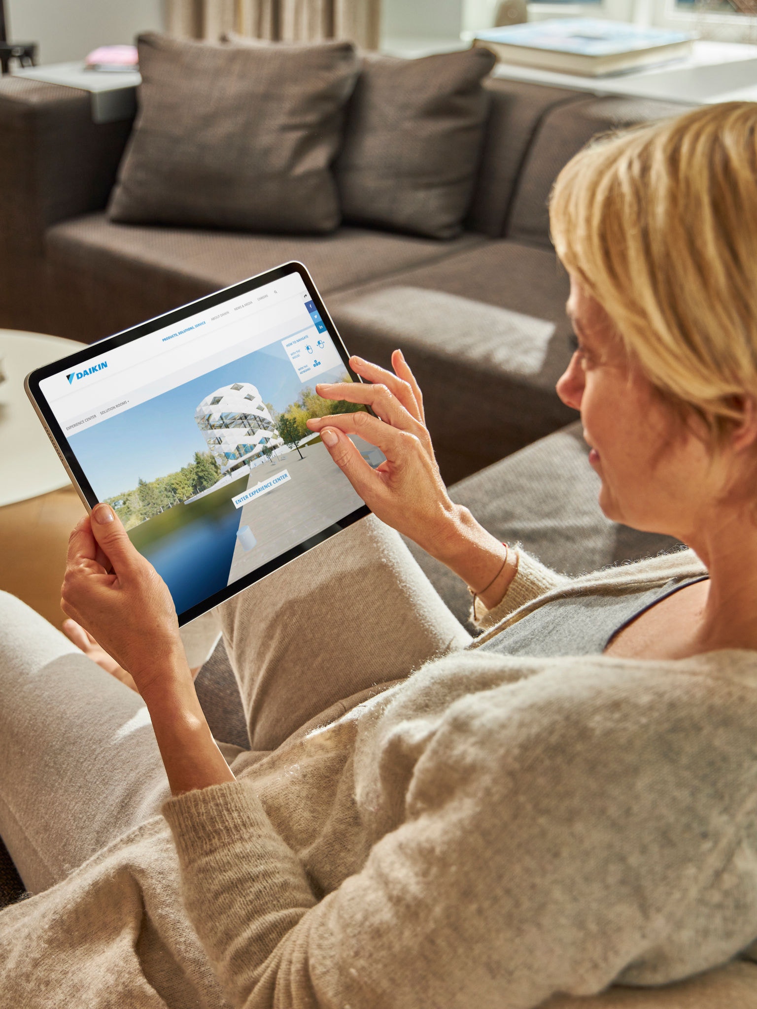 Ženska sedi na kavču in gleda klimatske naprave v središču za navidezne izkušnje na svoji tablici