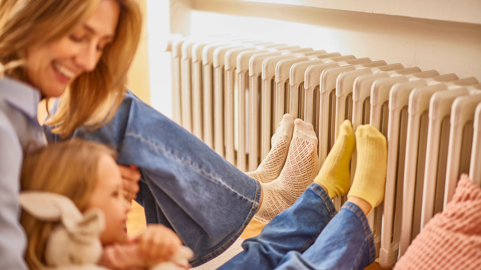 Mama in hči si grejeta noge na radiatorju v toplem ter udobnem domu