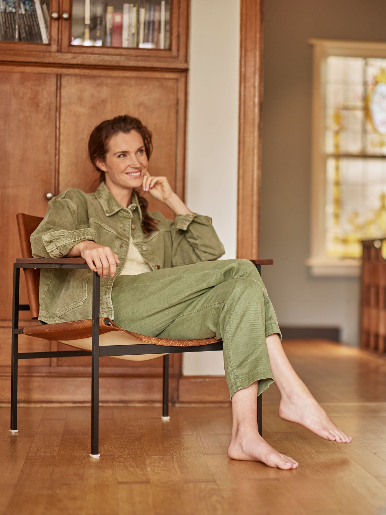 Ženska bosa sedi v naslanjaču, se smehlja in gleda naprej