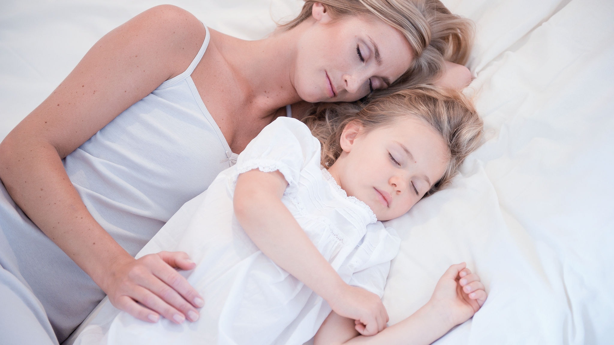 Mama in hčerkica spita druga ob drugi v beli postelji na čistem zraku