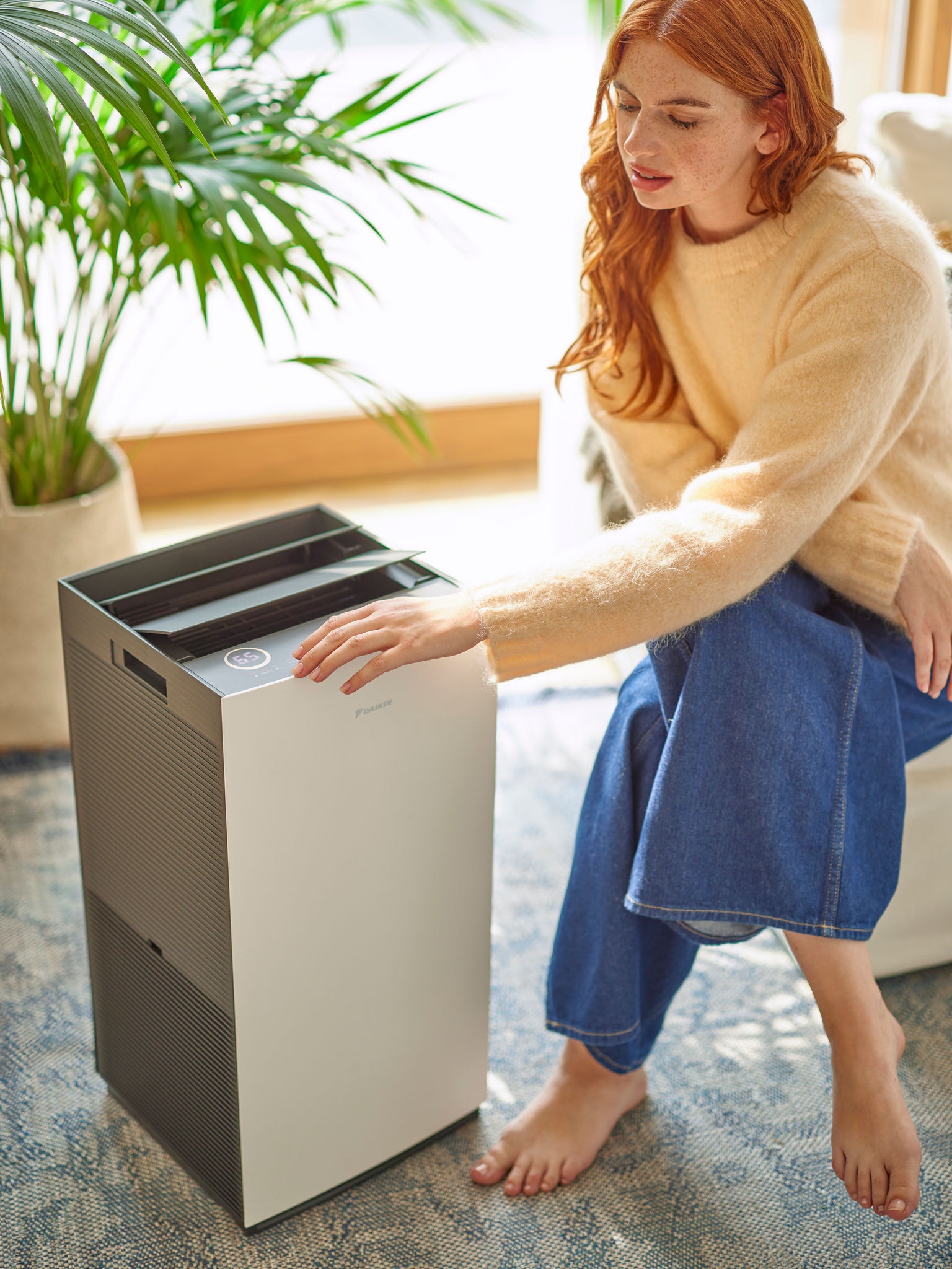 Ženska v dnevni sobi nastavlja upravljalne elemente čistilnika zraka Daikin