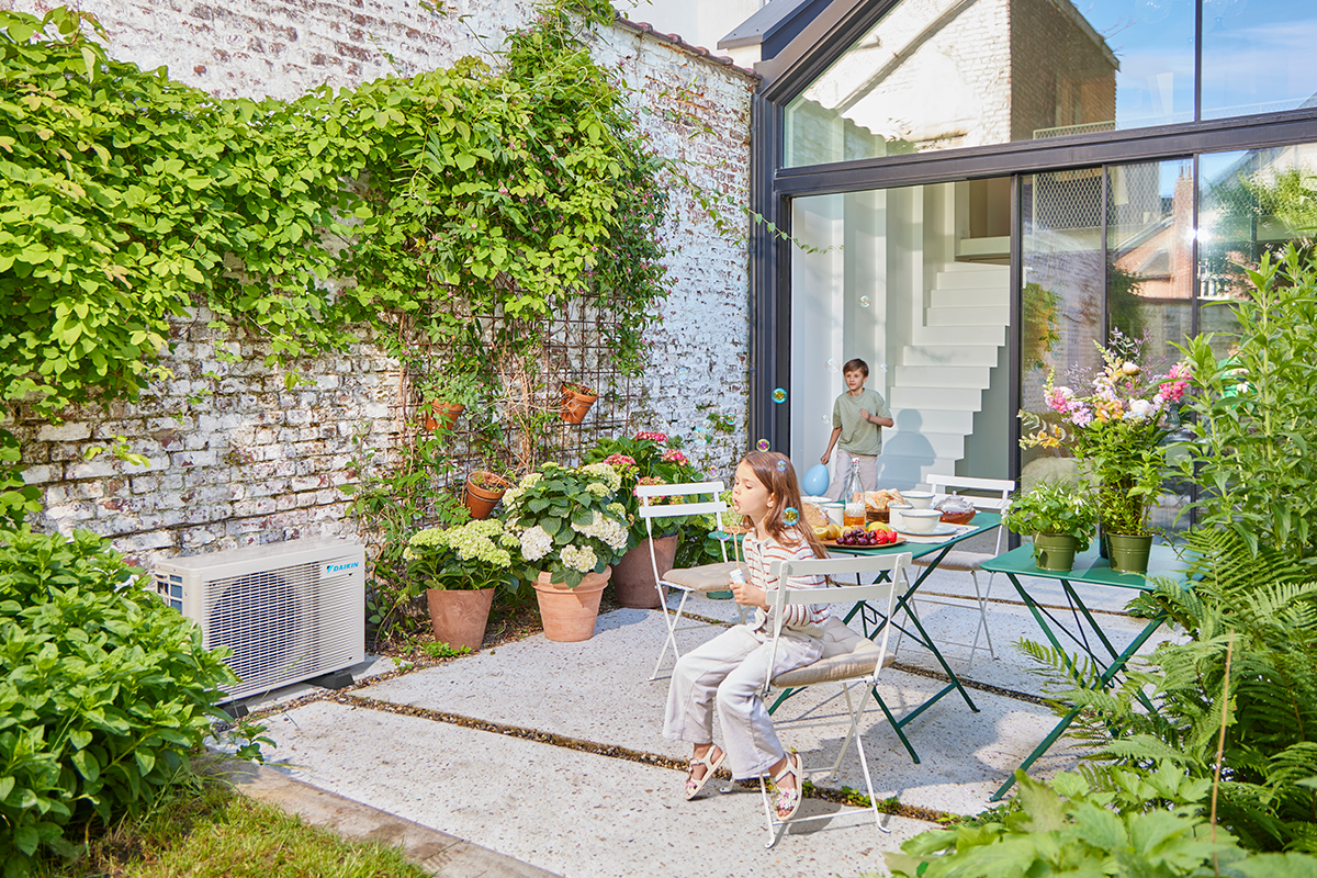 Otroci se igrajo s frnikolami na vrtni terasi poleg zunanje enote toplotne črpalke