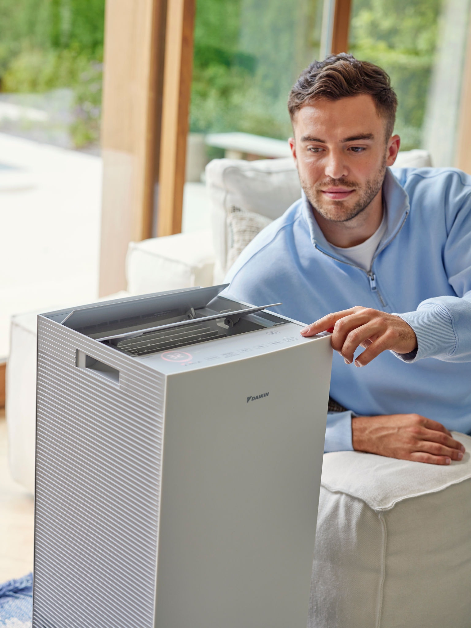 Moški nastavlja čistilnik zraka Daikin v dnevni sobi, da zmanjša alergene zaradi mačke