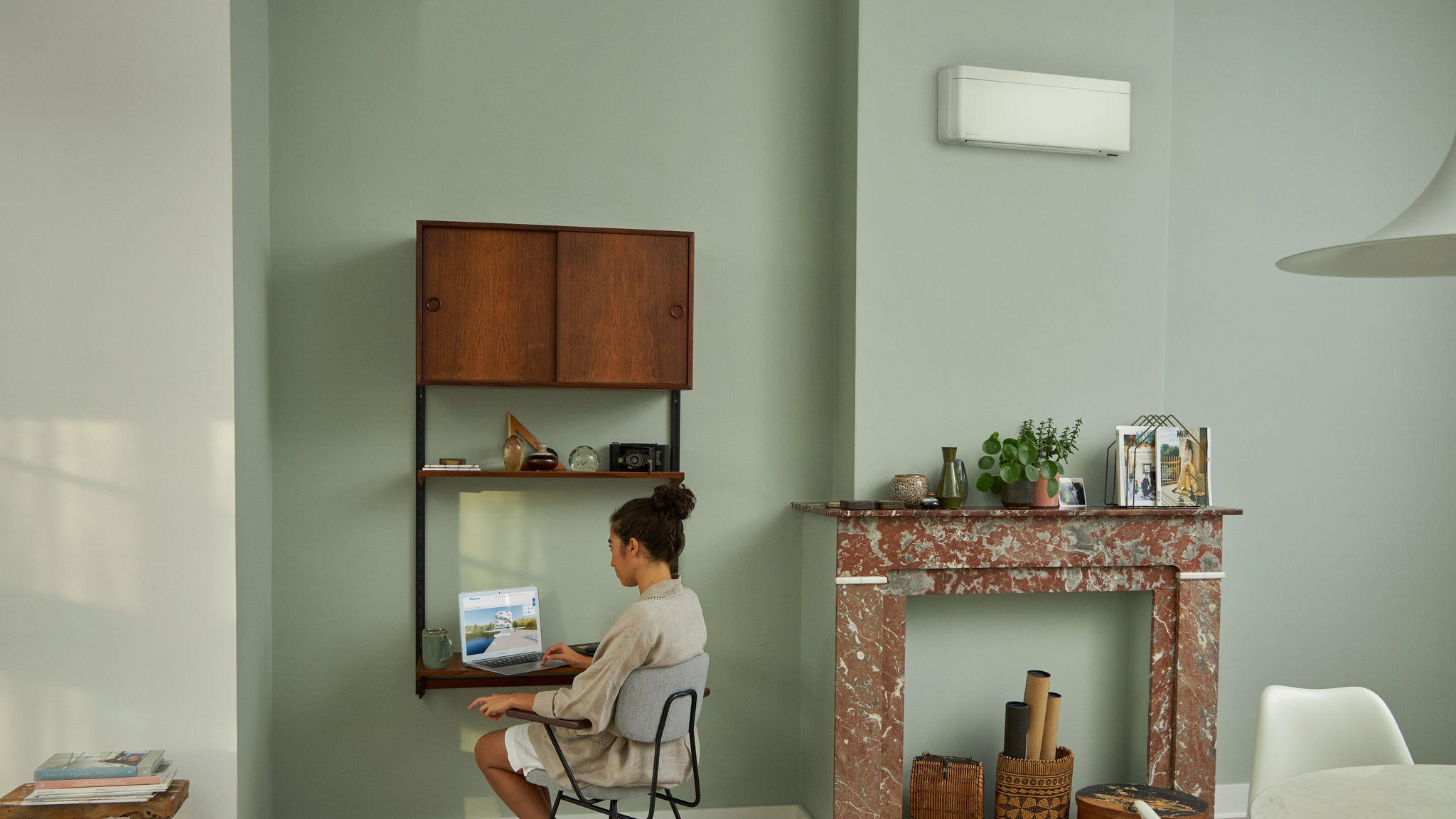 Ženska med obiskom navideznega izkustvenega središča Daikin na njenem prenosnem računalniku za svojo majhno pisalno mizo v lepo okrašeni dnevni sobi